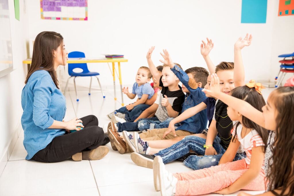 
Vista de perfil de um grupo de alunos da pré-escola levantando as mãos e tentando participar na escola.
